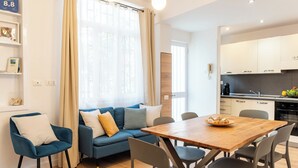 A modern living room with a sofa, chairs, a wooden dining table, and a kitchen area. - EIDOS - holiday house Taormina center (Taormina)