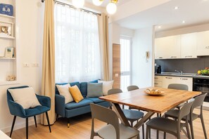 A modern living room with a sofa, chairs, a wooden dining table, and a kitchen area. - EIDOS - holiday house Taormina center (Taormina)