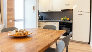 A modern kitchen with white cabinets, a wooden dining table, and a bowl of bread. - EIDOS - holiday house Taormina center (Taormina)