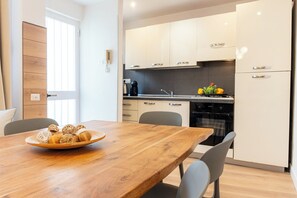 A modern kitchen with white cabinets, a wooden dining table, and a bowl of bread.