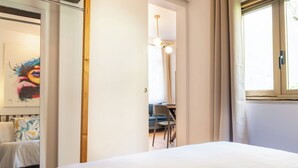 A bedroom with a bed, a desk, and a chair, a window with curtains, and a painting on the wall. - EIDOS - holiday house Taormina center (Taormina)