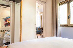 A bedroom with a bed, a desk, and a chair, a window with curtains, and a painting on the wall. - EIDOS - holiday house Taormina center (Taormina)
