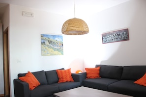 A modern living room with a dark grey sofa set, orange cushions, a woven pendant light, and two framed artworks on the walls. - A large farmhouse with views over Umbria/Tuscany with Aircon & streaming WiFi (Tuoro sul Trasimeno)