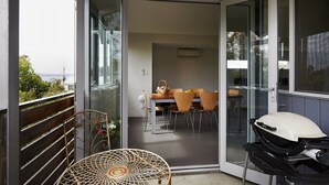 Una puerta corrediza de vidrio abierta que da a un comedor con una mesa, sillas y una parrilla.