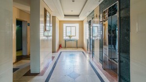 A hallway with a marble floor, a glass elevator, and a door with an emergency exit sign.