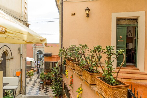 A narrow alley with a checkered floor, potted plants, and a yellow umbrella.