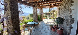 Une terrasse dallée de pierres, agrémentée de meubles en osier, de plantes en pot et offrant une vue sur un jardin aménagé.