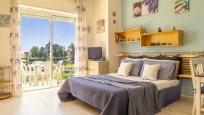 Un dormitorio con cama, televisor, balcón con sillas y obras de arte en las paredes.