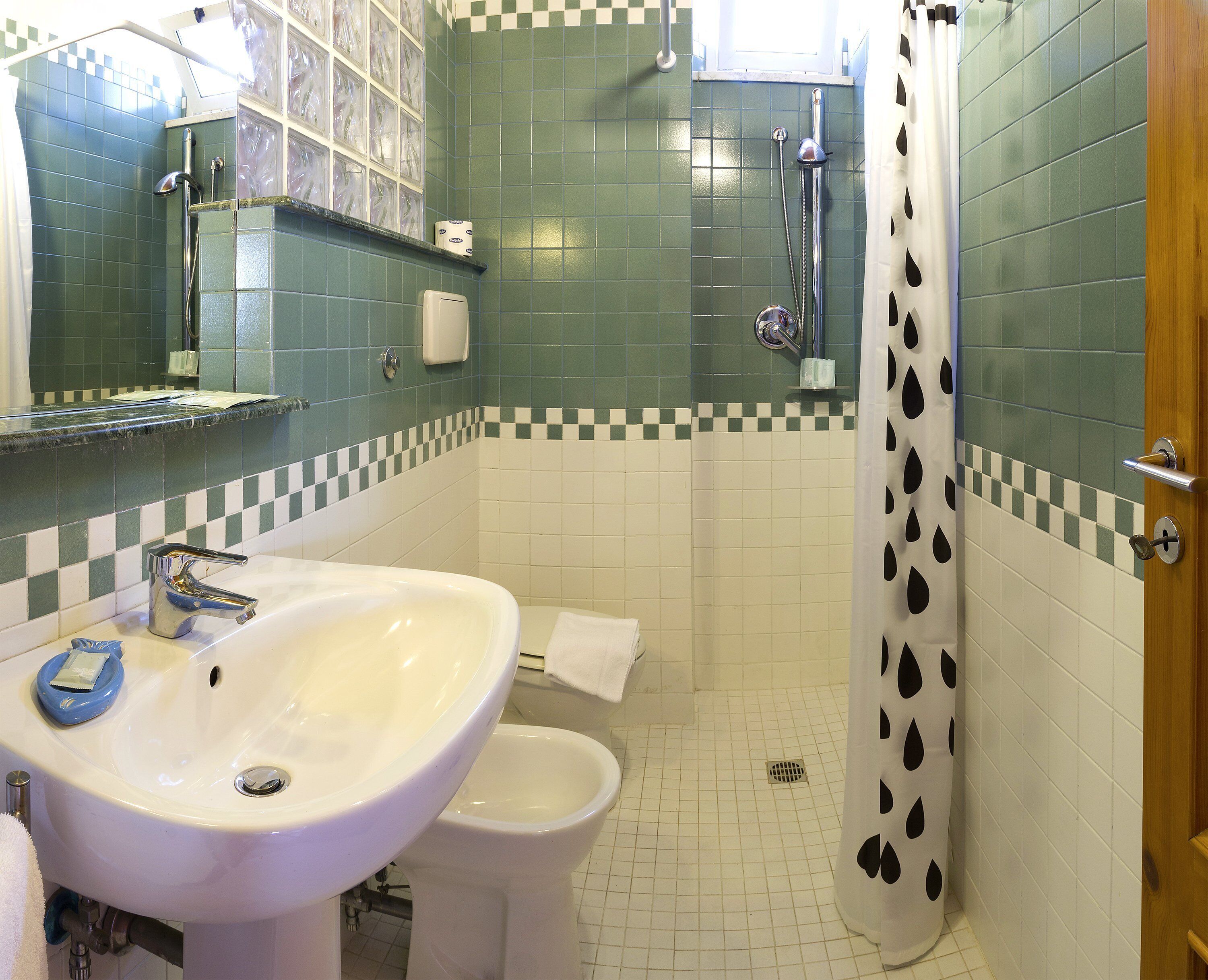 Ein Badezimmer mit einem weißen Waschbecken, einer Toilette und einer Dusche mit einem schwarz-weißen Vorhang mit Punkten.
