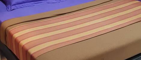 A bed with a striped mattress cover, a purple pillow, and a brown headboard.