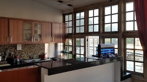 A kitchen with wooden cabinets, a stainless steel refrigerator, a coffee machine, and a large window with multiple panes. - Hotel DeQur Jakarta Kota (Jakarta)