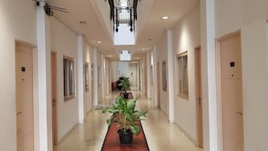 A long, well-lit hallway with doors on both sides, potted plants along the center, and a ceiling light fixture. - Hotel DeQur Jakarta Kota (Jakarta)
