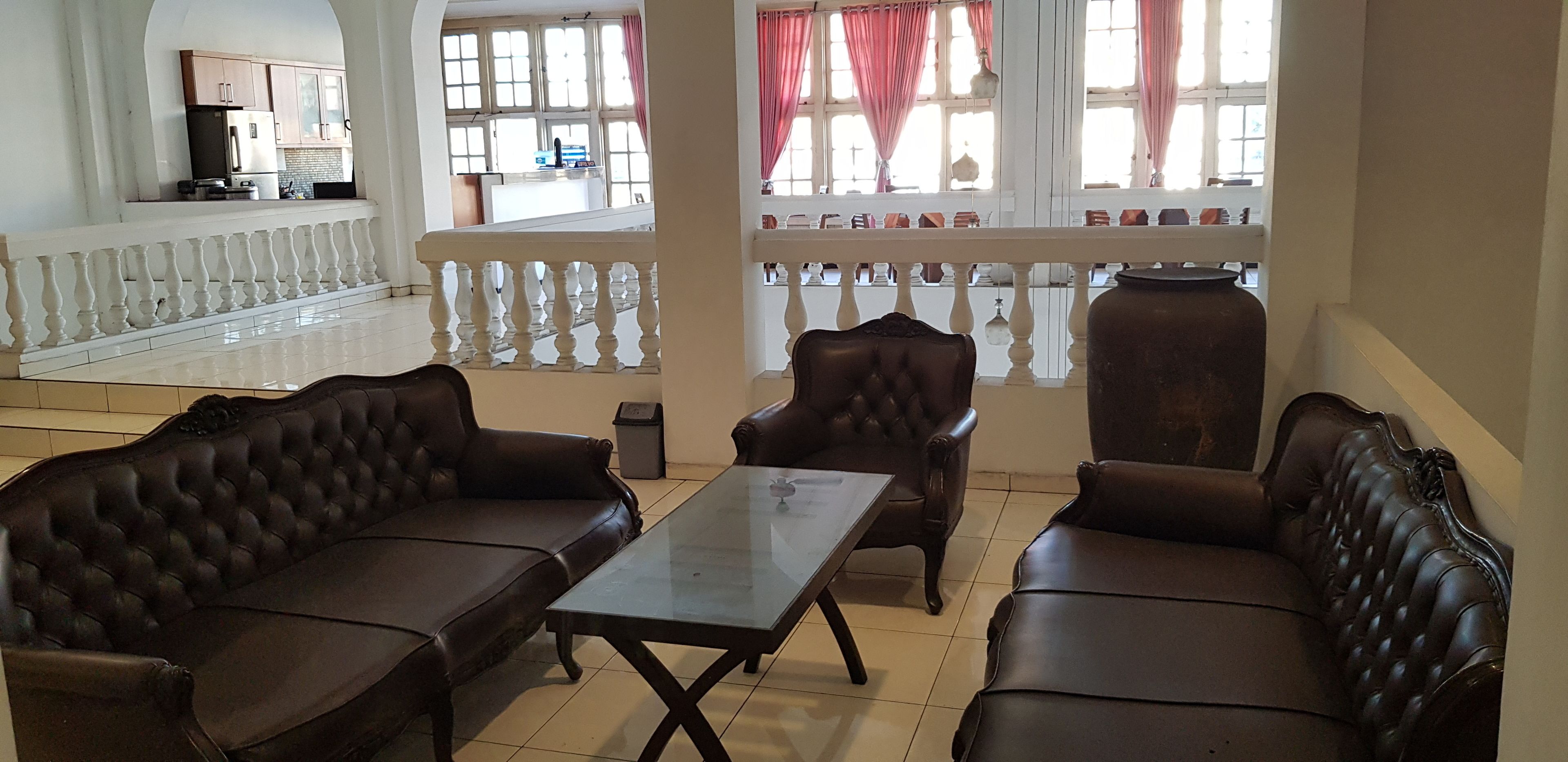 A spacious room with a balcony, leather sofas, a glass coffee table, and a kitchen area in the background.