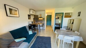 Un espace de vie compact comprenant un canapé, une table à manger et un coin cuisine en arrière-plan.
