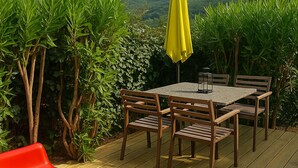 Une terrasse en bois avec une table et des chaises, un parasol jaune et des chaises rouges.