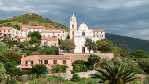 Une ville côtière qui se distingue par une église imposante, dotée d’un clocher et d’un dôme, et entourée de maisons à étages avec des toits de tuiles rouges.
