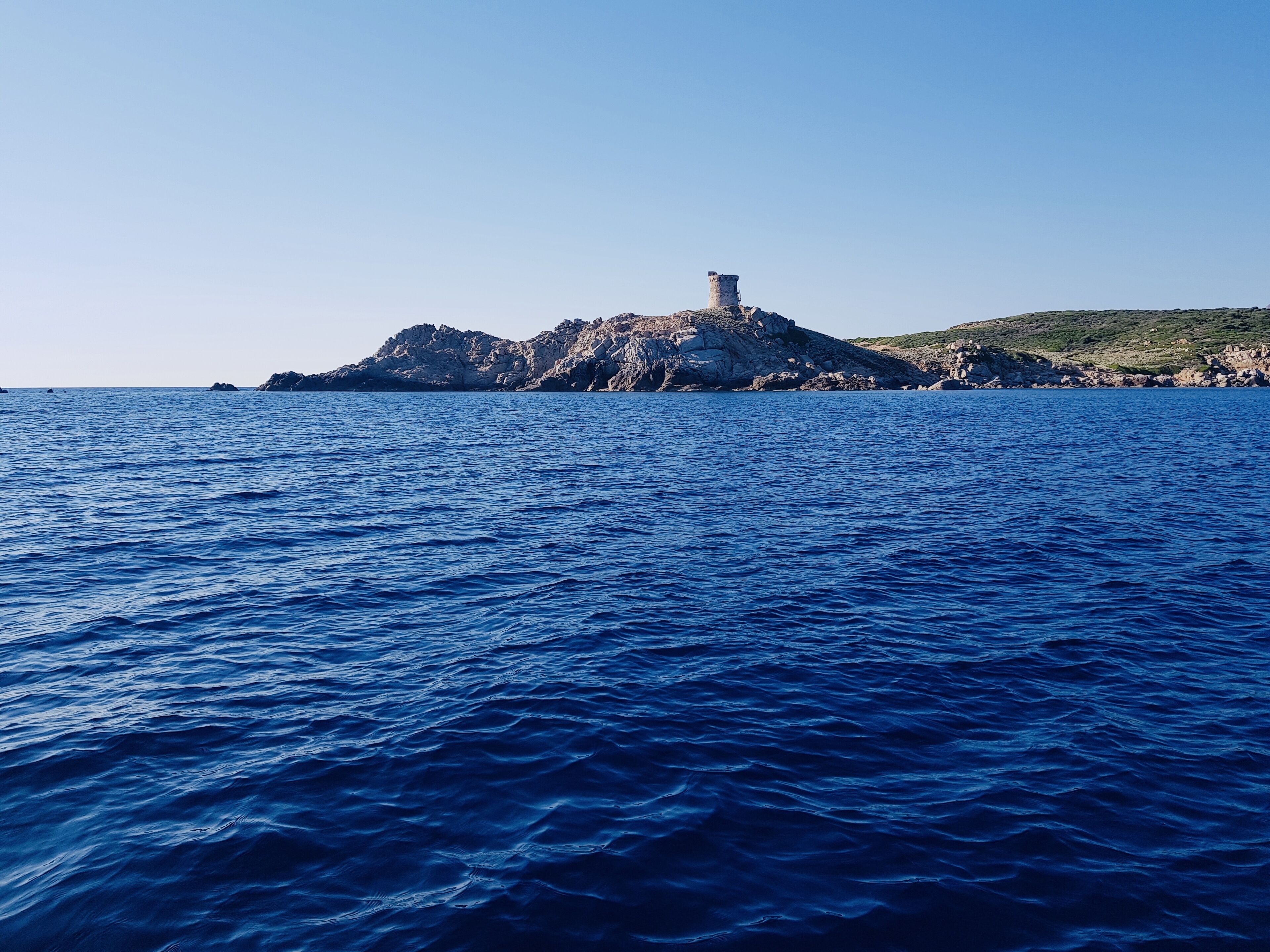 A rocky island with a tower in the middle of a calm sea.