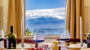 Une table dressée pour le dîner, avec vue sur une montagne enneigée et l’océan, à travers une fenêtre.