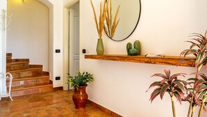 Un escalier avec une rampe en bois, un miroir fixé au mur et une étagère ornée d’objets décoratifs, notamment un cactus et un vase contenant des plantes séchées.
