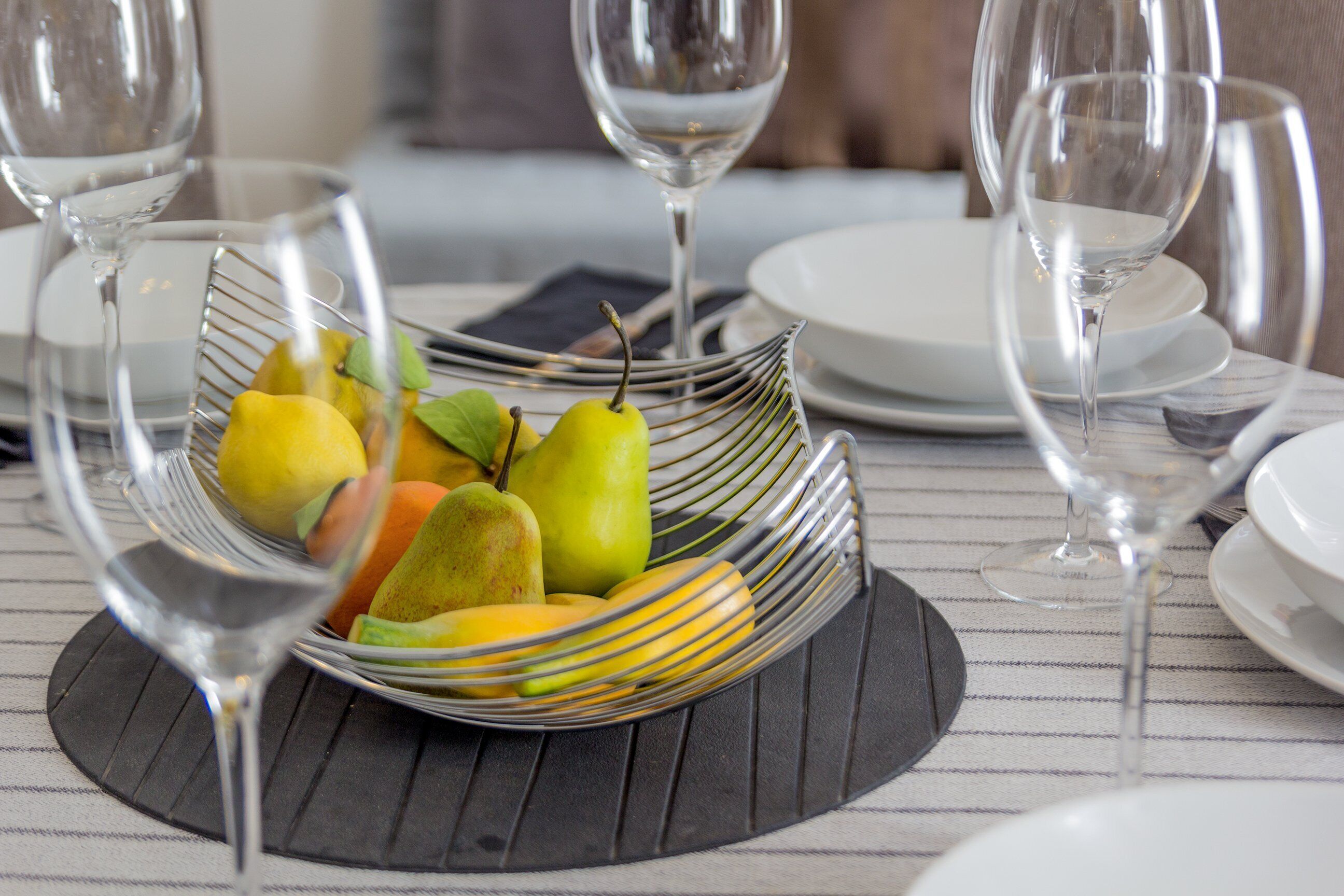 A dining table with a fruit bowl, wine glasses, and plates.