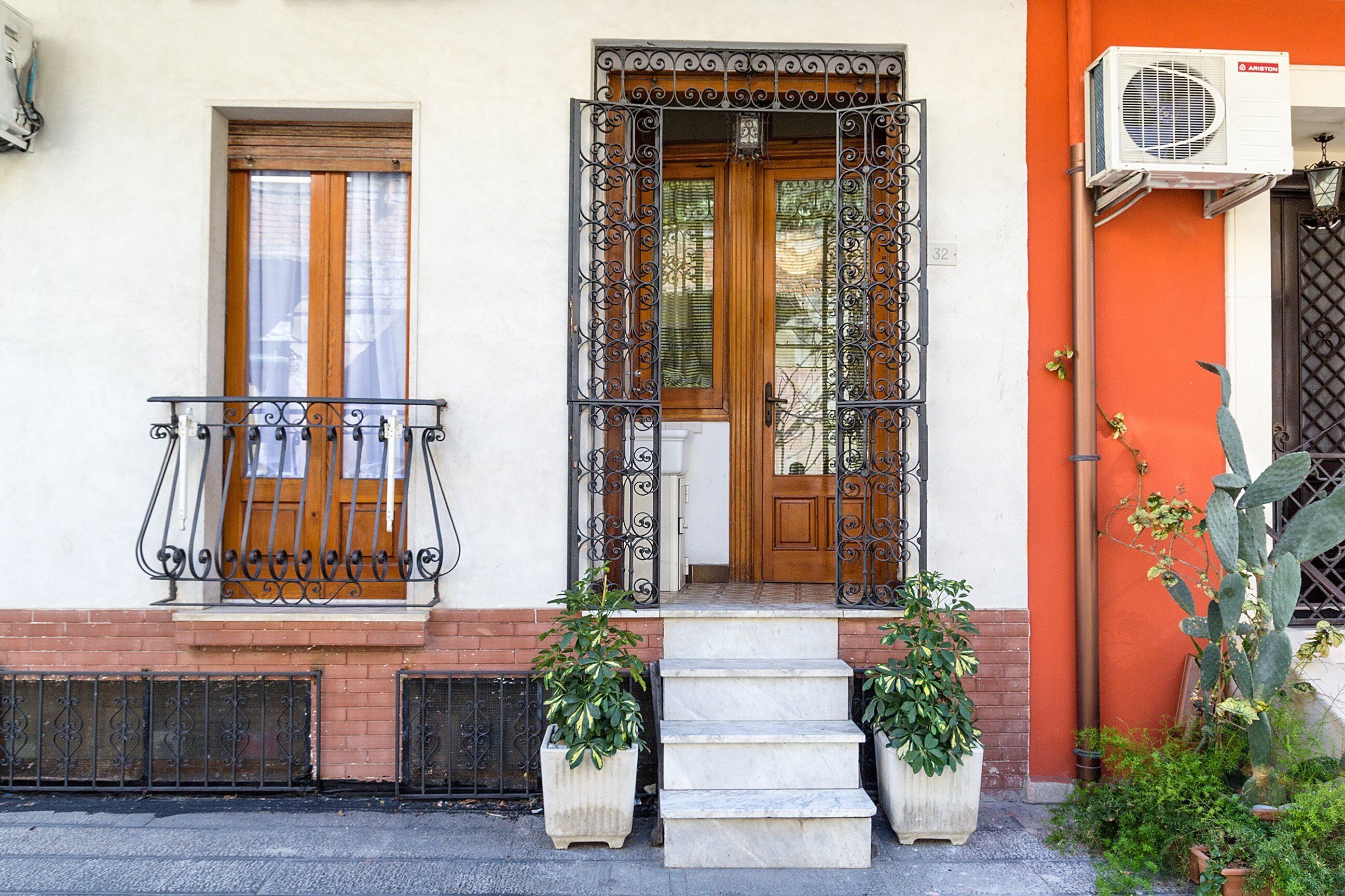 A building with a wooden door, a balcony with wrought iron railings, and a small garden area with potted plants.