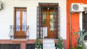 Un bâtiment doté d’une porte en bois, d’un balcon orné de balustrades en fer forgé et d’un petit jardin avec des plantes en pot.