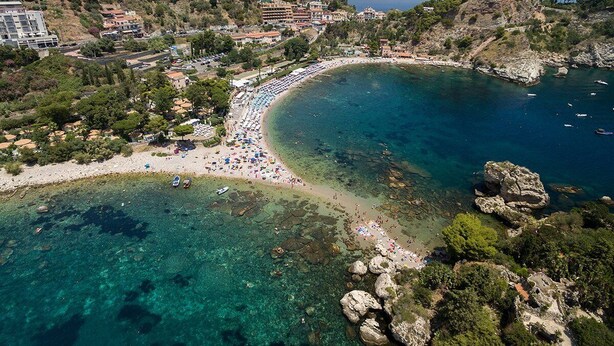 An aerial view of a coastal town with a beach, clear waters, rocky outcrops, and buildings. - TYSANDROS - SEA VIEW (Giardini-Naxos)