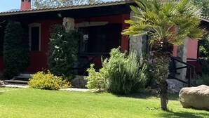 Una casa roja con chimeneas de piedra, un césped cuidado y diversas plantas.