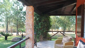 Un patio cubierto con mobiliario de mimbre, un pilar de piedra y vistas a la vegetación circundante.