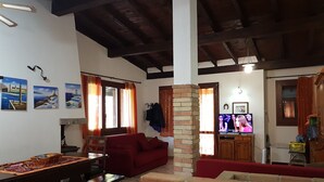 Una sala de estar con un sofá rojo, una mesa de madera y un televisor. Hay cuadros en la pared y un pilar de ladrillo.