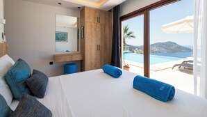 Een hotelkamer met een bed, een groot raam met uitzicht op de zee, een houten garderobe en een klein tafeltje met een blauwe handdoek.