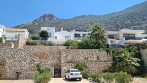 Eine moderne Villa mit Steineinfahrt, einem geparkten Auto davor und einem Berg im Hintergrund.