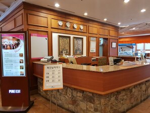 Zona de recepción de un hotel con mostrador de piedra, relojes mostrando la hora en varias ciudades y un cartel que indica las temperaturas de las habitaciones.