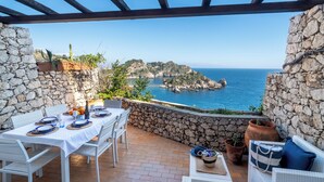 A terrace with stone walls, a table set for dining, and a view of the sea and rocky landscape. - Sea Life Taormina - Infinity pool (Taormina)