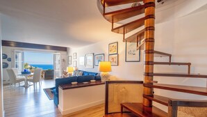 A spacious living area with a wooden staircase, a blue sofa, and a dining table with chairs. - Sea Life Taormina - Infinity pool (Taormina)
