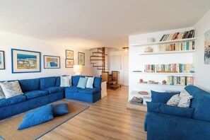 A living room with two blue sofas, a wooden floor, and a spiral staircase.