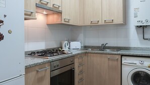 A compact kitchen with wooden cabinets, a built-in oven, a microwave, a dishwasher, and a washing machine. - Cozy Flat with Unbeatable Views of Sagrada Familia (Barcelona)