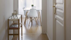 A hallway leading to a dining area with a table and chairs, a potted plant, and a wooden chair with books. - Cozy Flat with Unbeatable Views of Sagrada Familia (Barcelona)