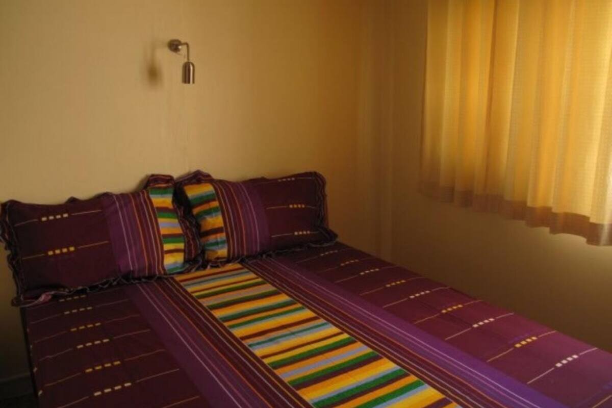 A single bed with striped bedding, a wall-mounted light, and a window with curtains.
