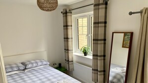 A bedroom with a bed, a window with curtains, a radiator, a small table with a plant, and a mirror. - Centre of Town, 3 bedrooms, sleeps 6, own parking and patio close to The Oracle (Reading)
