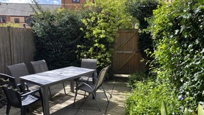A patio with a table and chairs, surrounded by greenery and a wooden fence. - Centre of Town, 3 bedrooms, sleeps 6, own parking and patio close to The Oracle (Reading)
