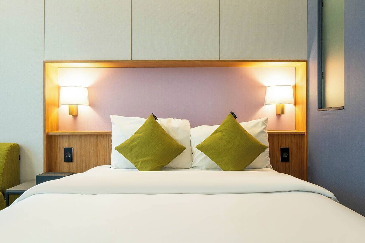A hotel room with a bed, two bedside lamps, and a nightstand.