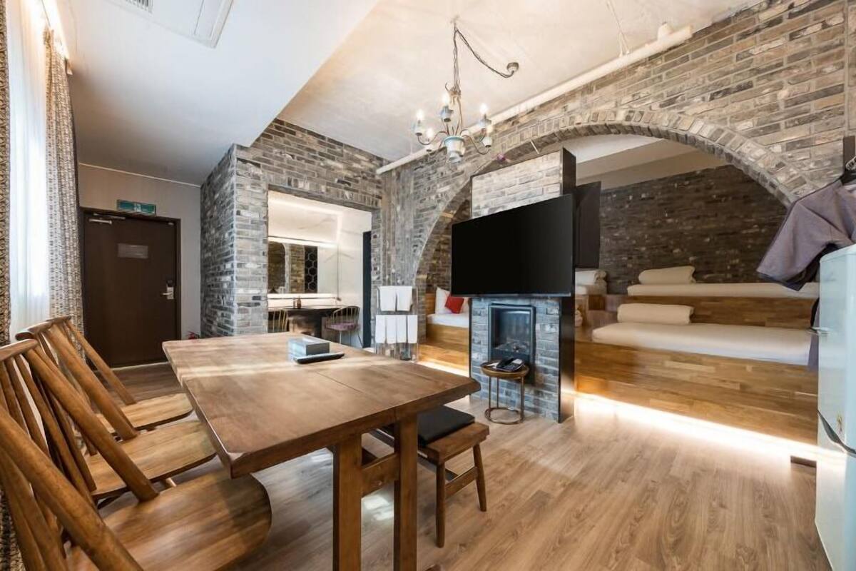 A cozy living area with a fireplace, a TV mounted on a brick wall, and a dining table with chairs.