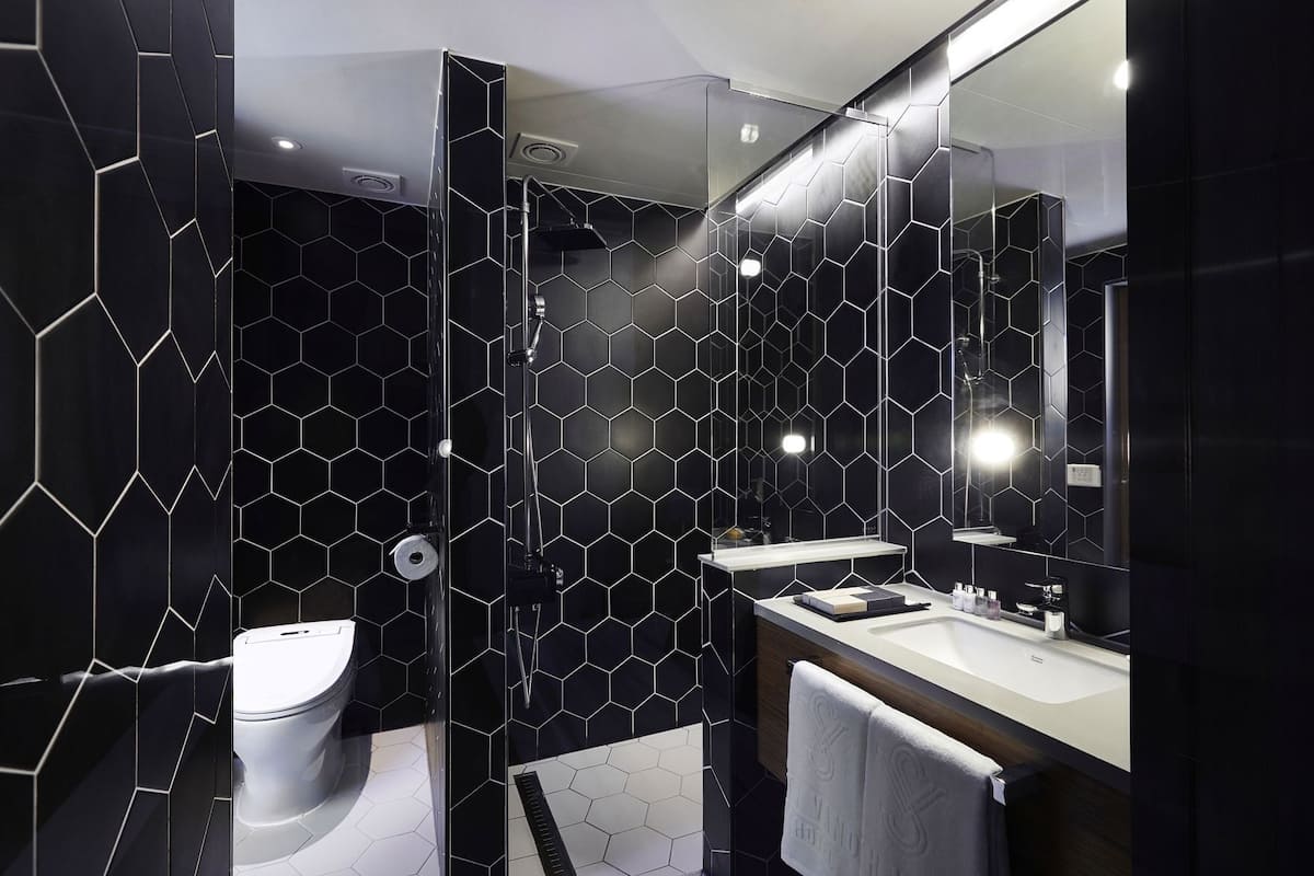 A modern bathroom with a black hexagonal tile wall, a white toilet, a sink with a mirror, and a towel rack.
