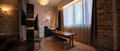 Una cocina moderna con una mesa y un banco de madera, una lámpara colgante y vistas de la ciudad a través de amplias ventanas con cortinas translúcidas.