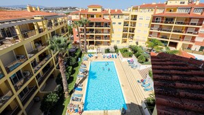 Un hotel de varios pisos con una piscina central rodeada de tumbonas y palmeras.