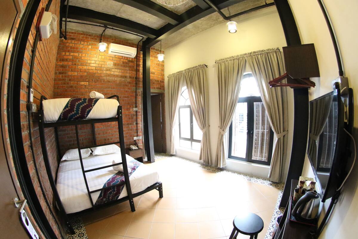 A room with a bunk bed, a desk, a chair, a television, and a window with curtains.