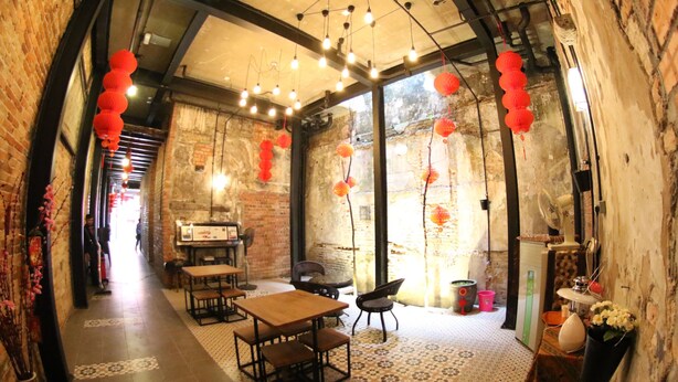 A narrow, brick-walled corridor with tables and chairs, red lanterns, and a fan on a shelf. - Ban Loong Hotel (Ipoh)