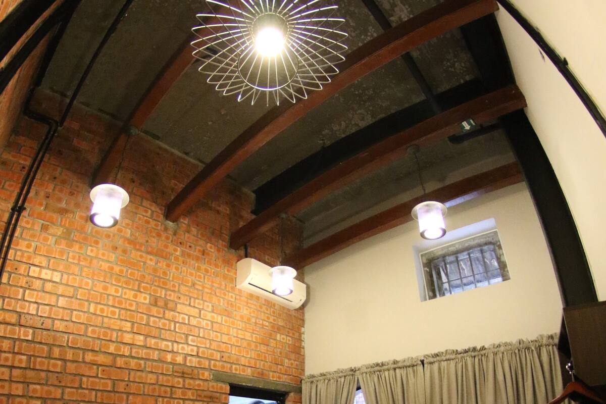 A hotel room with a brick wall, a bed with white linens, a hanging light fixture, and a small window with curtains.