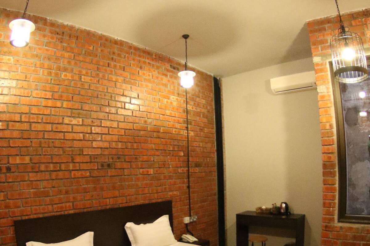 A room with two beds, a brick wall, a hanging light fixture, and a small table.